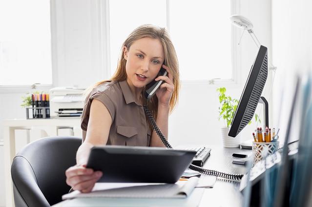 Kobieta pracująca przy biurku, rozmawiająca przez telefon i patrząca w tablet